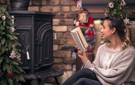 girl reading a book in a cozy home atmosphere near the fireplace, the concept of home restの写真素材