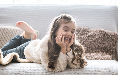 happy little girl lying on the couch, beautiful smile, rest conceptの写真素材