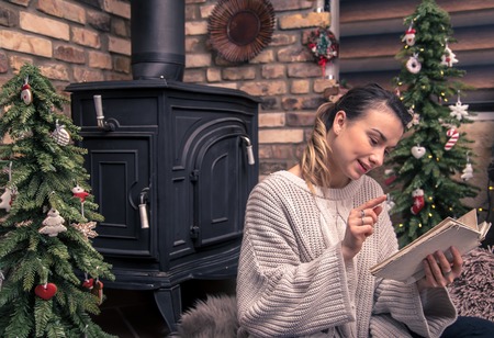 girl reading a book in a cozy home atmosphere near the fireplace, the concept of home restの写真素材