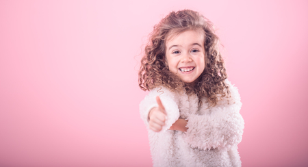 Portrait of a cute little smiling girl with curly hair pointing up on a pink backgroundの写真素材