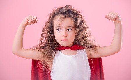 Kids concept, frustrated kinky girl playing super hero, shows her strength, isolated on pink backgroundの写真素材