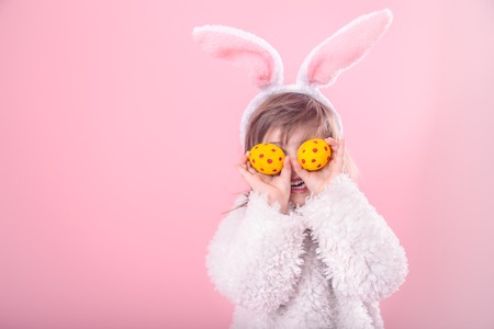 Portrait of cute little girl with Bunny ears and yellow Easter eggs in red polka dots, closes eyes with testicles, isolated on pink backgroundの写真素材