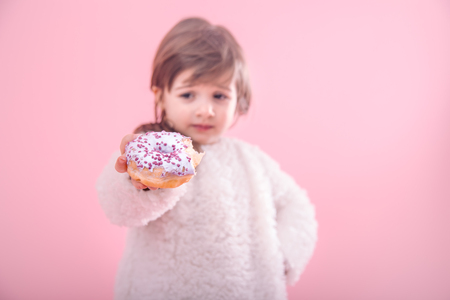 Portrait of a little girl with a donut in her hands isolated on pink backgroundの写真素材