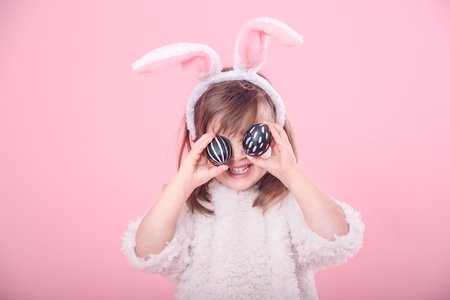Portrait of a cute little girl with Bunny ears and Easter eggs, isolated on pink backgroundの写真素材