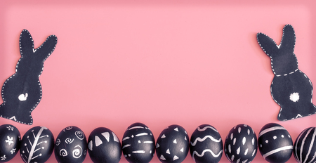Easter composition from eggs of the black colors with creative light pattern, handmade in a round nest made of hay ,and the Easter Bunny in black colour isolated on pink background , the concept of the Easter holidaysの写真素材