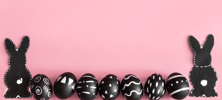 Easter composition from eggs of the black colors with creative light pattern, handmade in a round nest made of hay ,and the Easter Bunny in black colour isolated on pink background , the concept of the Easter holidaysの写真素材