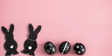 Easter composition from eggs of the black colors with creative light pattern, handmade in a round nest made of hay ,and the Easter Bunny in black colour isolated on pink background , the concept of the Easter holidaysの写真素材