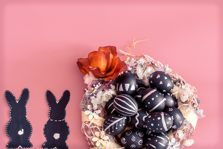 Easter composition from eggs of the black colors with creative light pattern, handmade in a round nest made of hay ,and the Easter Bunny in black colour isolated on pink background , the concept of the Easter holidaysの写真素材