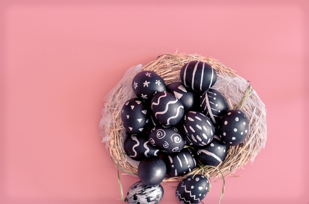 Easter composition from eggs of the black colors with creative light pattern, handmade in a round nest of hay isolated on a pink background , the concept of the Easter holidaysの写真素材