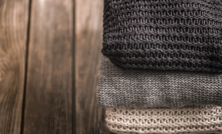 a stack of knitted sweaters in white, gray and black on a wooden background, close-up, space for textの写真素材