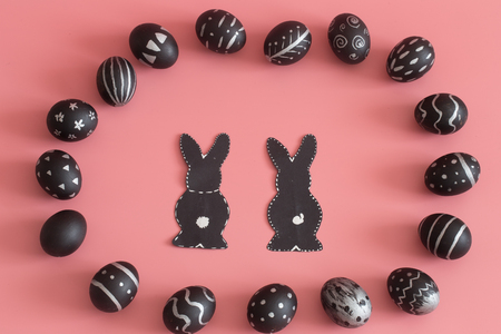 Easter composition from eggs of the black colors with creative light pattern, handmade in a round nest made of hay ,and the Easter Bunny in black colour isolated on pink background , the concept of the Easter holidaysの写真素材