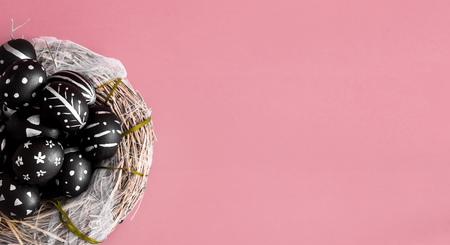 Easter background with eggs in black with a bright pattern handmade in nest of hay on a pink backgroundの写真素材