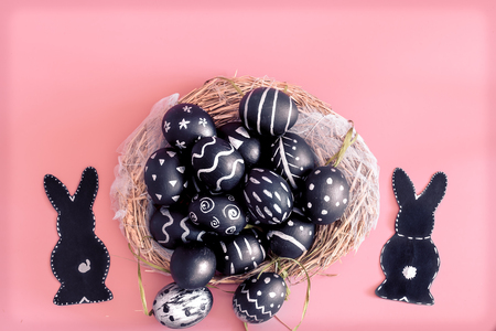 Easter composition from eggs of the black colors with creative light pattern, handmade in a round nest made of hay ,and the Easter Bunny in black colour isolated on pink background , the concept of the Easter holidaysの写真素材