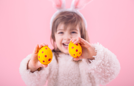 Portrait of a cute little girl with Bunny ears and yellow Easter eggs in red polka dots isolated on pink backgroundの写真素材