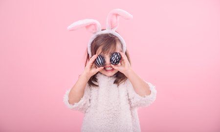 Portrait of a cute little girl with Bunny ears and Easter eggs, isolated on pink backgroundの写真素材