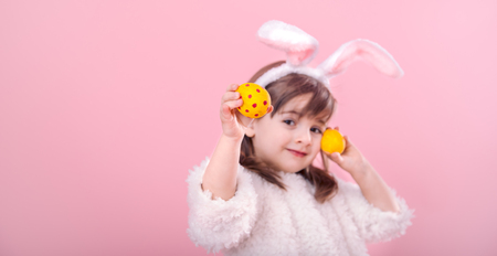 Portrait of a cute little girl with Bunny ears and yellow Easter eggs in red polka dots isolated on pink backgroundの写真素材
