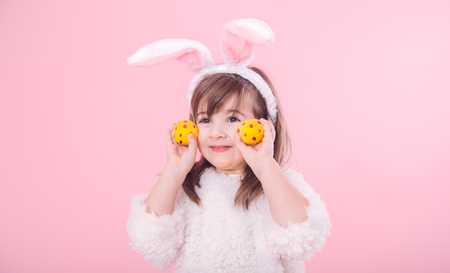 Portrait of a cute little girl with Bunny ears and yellow Easter eggs in red polka dots isolated on pink backgroundの写真素材