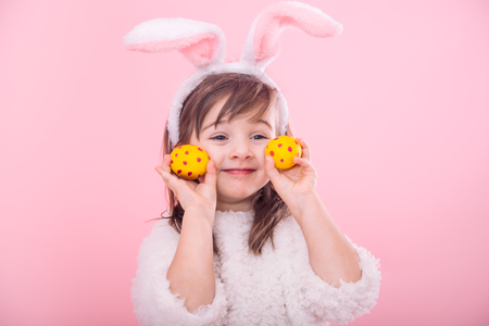 Portrait of a cute little girl with Bunny ears and yellow Easter eggs in red polka dots isolated on pink backgroundの写真素材