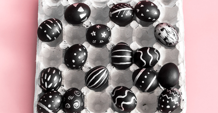 Easter background with black eggs with bright handmade pattern in tray on pink backgroundの写真素材