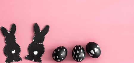 Easter composition from eggs of the black colors with creative light pattern, handmade in a round nest made of hay ,and the Easter Bunny in black colour isolated on pink backgroundの写真素材