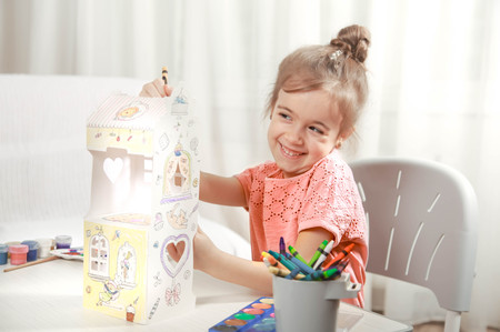 A cute little girl is painting a paper house with colored pencils in a homely atmosphere. The concept of child development and family.の写真素材