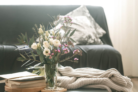 Cozy home interior living room with a black sofa and a vase with flowers and decor items on a small tableの写真素材