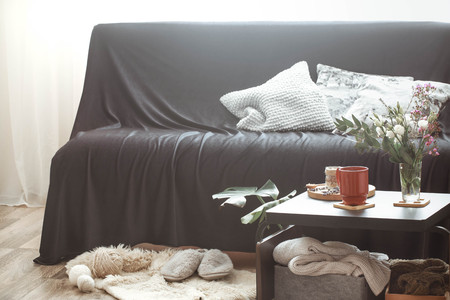 Cozy home interior living room with a black sofa and a vase with flowers and decor items on a small tableの写真素材