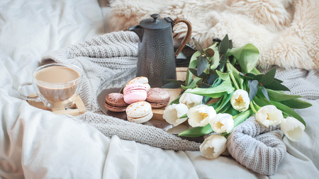 Still-life morning breakfast with coffee and macaroon on the background of a bed with white tulips, concept of women's dayの写真素材