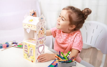 A cute little girl is painting a paper house with colored pencils in a homely atmosphere. The concept of child development and family.の写真素材