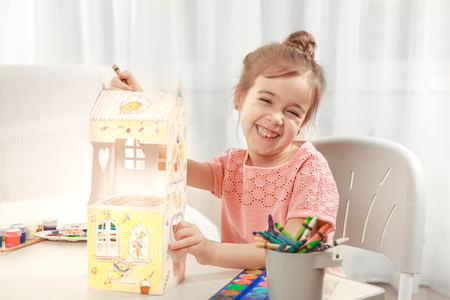 A cute little girl is painting a paper house with colored pencils in a homely atmosphere. The concept of child development and family.の写真素材