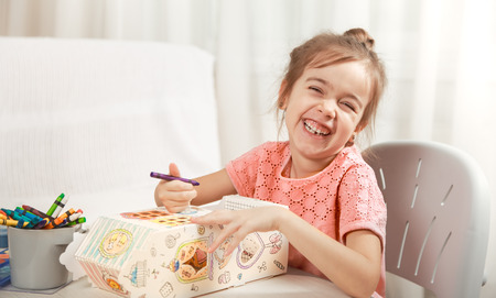 A cute little girl is painting a paper house with colored pencils in a homely atmosphere. The concept of child development and family.の写真素材