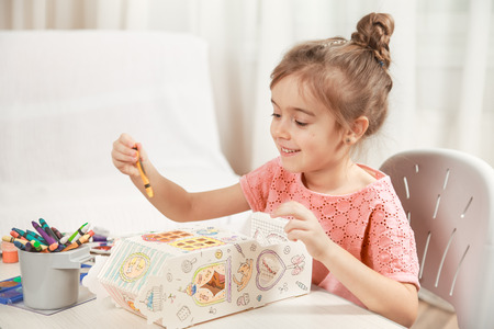 A cute little girl is painting a paper house with colored pencils in a homely atmosphere. The concept of child development and family.の写真素材