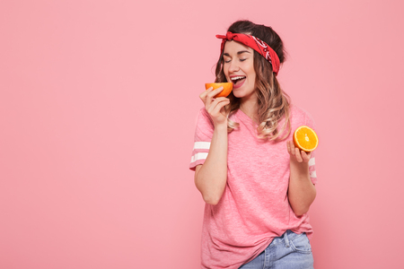 Horizontal portrait of hipster girl in stylish clothes with oranges in their hands, healthy food, on pink background, lifestyle conceptの写真素材