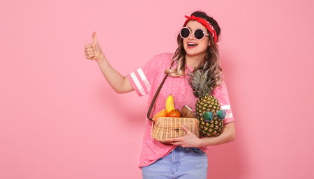 Horizontal portrait of hipster girl in stylish clothes with sunglasses, with healthy food, fruits, on pink background, lifestyle conceptの写真素材