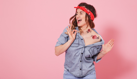 Horizontal portrait of hipster girl in jeans clothes with tattoo on body, on pink background, lifestyle conceptの写真素材