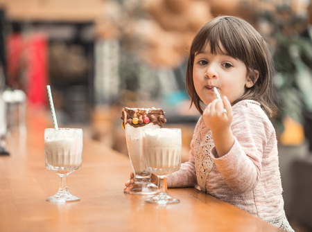 Charming Funny little girl drinks a milkshake in a restaurant, licking a tube. Baby food fast food . Leisure in the cafe.の写真素材