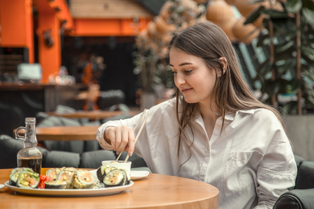 Young Woman eating and enjoying fresh sushi in luxury restaurant. Female client holding food sticks and eating oriental meal on lunch. Concept of food.の写真素材