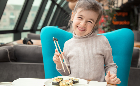 Charming funny girl eating sushi in a restaurant. Fast food. Leisure in the cafe. The concept of foodの写真素材