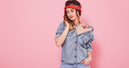 Horizontal portrait of hipster girl in jeans clothes with tattoo on body, on pink background, lifestyle conceptの写真素材