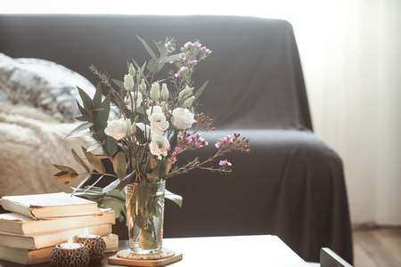 Cozy home interior with elements of decor in the living room with a black sofa and a vase of flowers and lighted candles on a small tableの写真素材