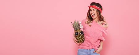 Beautiful young girl in pink t-shirt with decal water tattoo sticker, smiling with pineapple on pink background. Place for text. Advertising conceptの写真素材