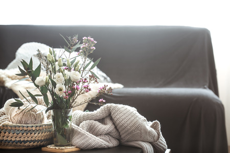 Cozy home interior living room with a black sofa and a vase with flowers and decor items on a small tableの写真素材