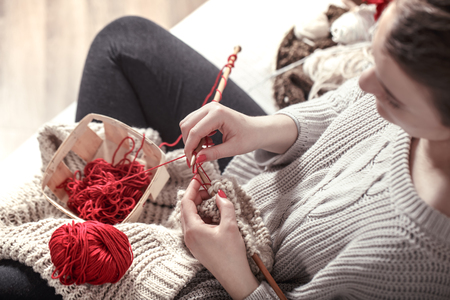 wooden spokes and red yarn in the hands of a woman on a cozy sofa . Still life photo. The concept of comfortの写真素材