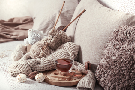 Vintage wooden spokes and yarn on a cozy sofa with a sweater and a Cup of tea . Still life photo. The concept of comfortの写真素材