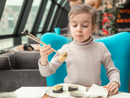 Charming funny girl eating sushi in a restaurant. Fast food. Leisure in the cafe. The concept of foodの写真素材
