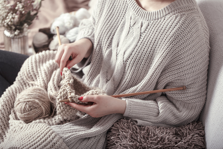 Vintage wooden spokes and yarn in the hands of a woman on a cozy sofa . Still life photo. The concept of comfortの写真素材