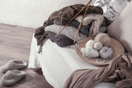 Vintage wooden knitting needles and threads on a cozy sofa with pillows and Slippers nearby. Still life photo. The concept of comfortの写真素材
