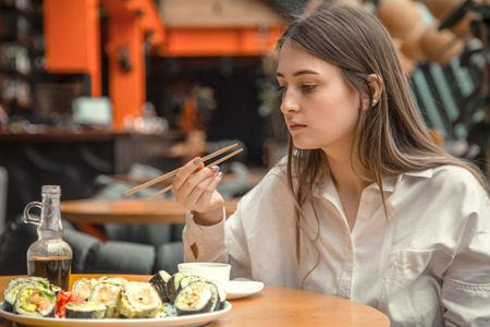Young Woman eating and enjoying fresh sushi in luxury restaurant. Female client holding food sticks and eating oriental meal on lunch. Concept of food.の写真素材