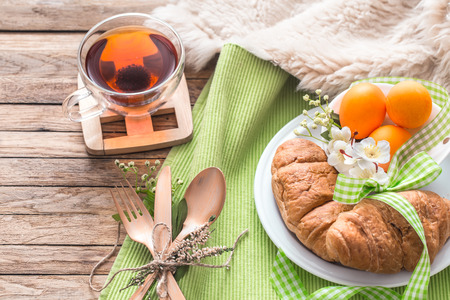 Easter breakfast with croissants and tea with colorful Easter eggs in a plate on wooden backgroundの写真素材