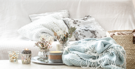 Home decorations in the interior. On the wooden background lies a turquoise blanket and wicker basket with a vase of flowers and candles. Concept of comfortの写真素材